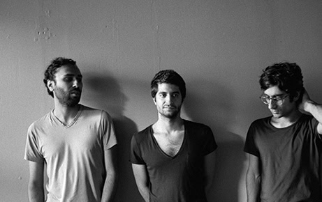 The three members of Dawn of Midi stand against a plain wall, captured in a black-and-white photo with a relaxed, introspective mood.