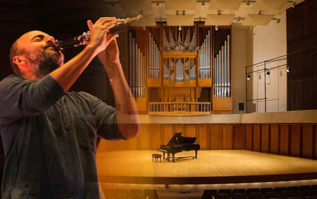 Clarinetist Kinan Azmeh passionately plays against a blended background image of an empty concert hall stage with a grand piano and organ pipes.