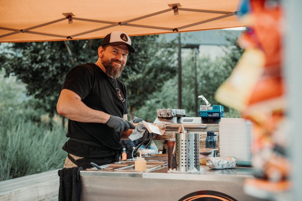 A smiling vendor prepares food at the 2024 Nebraska Crossroads Music Festival at Gene Leahy Mall in Omaha