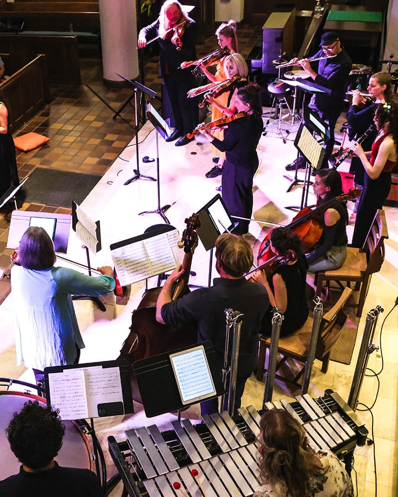Looking down from above on a chamber orchestra of musicians performing standing up.