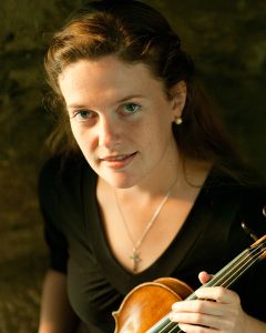 Violinist Fiona Hughes holding her instrument, in soft lighting with a natural background