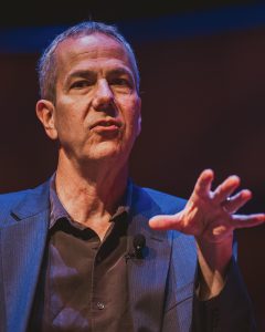 Poet Matt Mason speaking on stage with a microphone, gesturing expressively