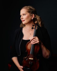 Susanna Gilmore holding a violin, portrait in black outfit against a dark background