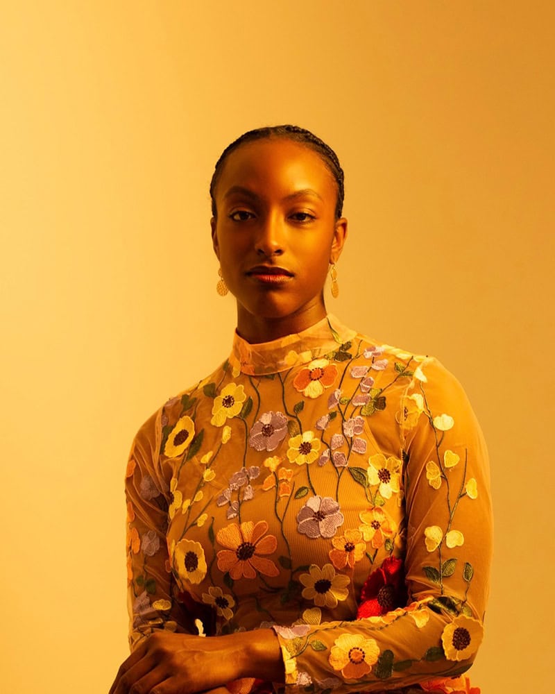 Poet Jewel Rodgers in a floral embroidered top, seated against a warm golden background