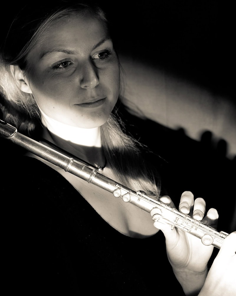 Flutist Marie Sønderskov in soft lighting, holding her flute while gazing thoughtfully to the side