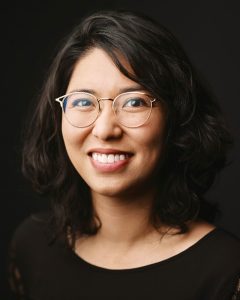 Juliet Yoshida smiling in a black blouse against a dark background