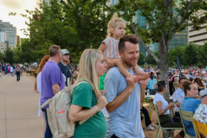 A small girl rides on her father's shoulders as their mother looks towards the stage at the 2023 Omaha Showcase.