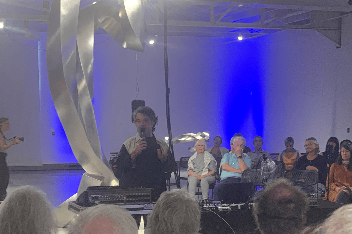 Erdem Helvacioglu speaks to the audience after KANEKO performance in front of a large metal statue