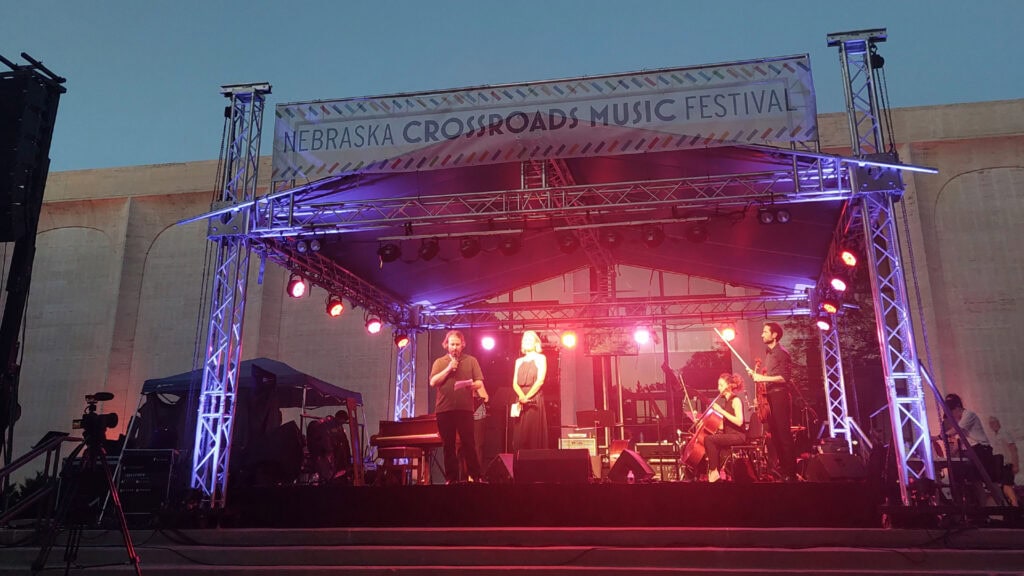 An outdoor stage lit up by purple and red lights. Erik Higgins speaks into the microphone