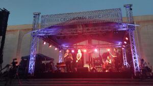 An outdoor stage lit up by purple and red lights. Erik Higgins speaks into the microphone
