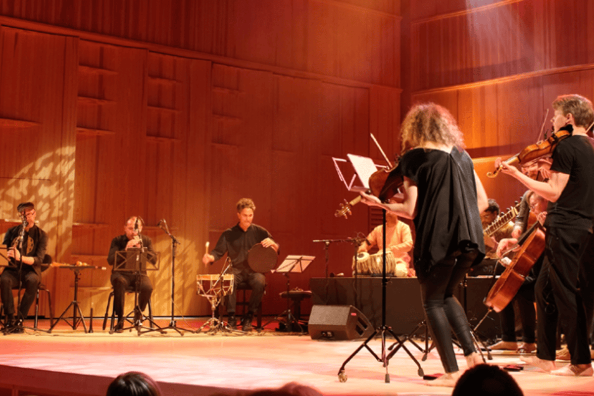 Musicians perform on a large wooden stage with red lighting.