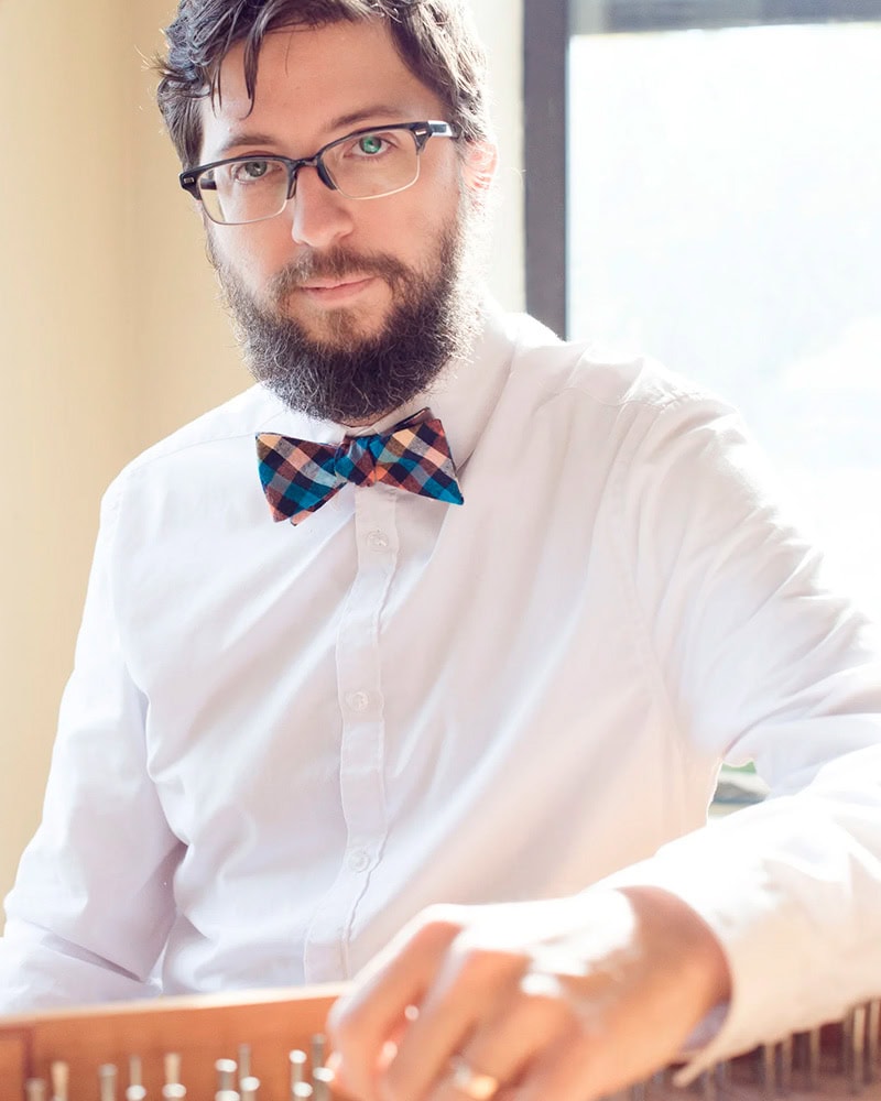 Gabe Shuford, wearing white shirt and bowtie, hand on harpsichord